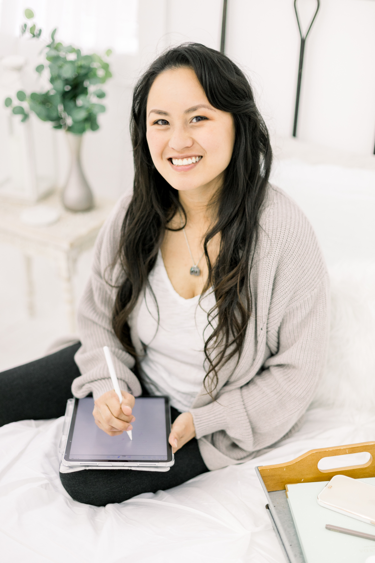 Serena Kretchmer smiling on a bed, writing on a tablet with a stylus.