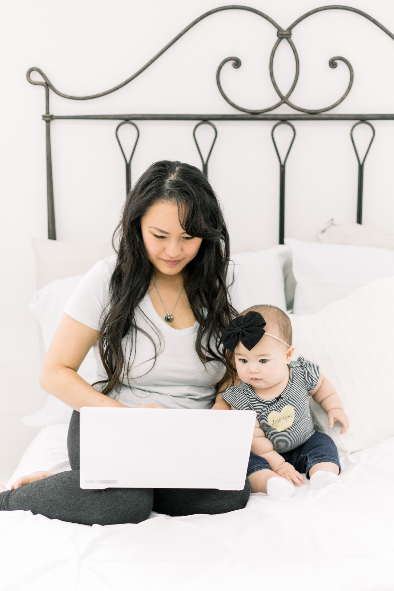 Serena Kretchmer on a bed with her laptop, her baby sitting beside her.